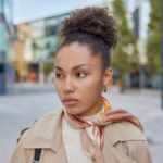 thoughtful-woman-with-curly-combed-hair-wears-coat-kerchief-tied-neck-concentrated-away-poses-against-blurred-street-background-pretty-female-model-explores-new-city-pastime_273609-60615